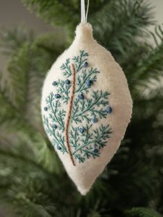 an ornament hanging from a christmas tree decorated with blue and green leaves on it