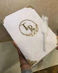 a person holding up a wedding album with a feather on the front and bottom cover