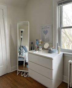 a white dresser sitting in front of a window next to a mirror and radiator