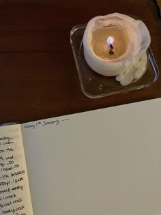 an open book with a lit candle on it next to a notepad and pen