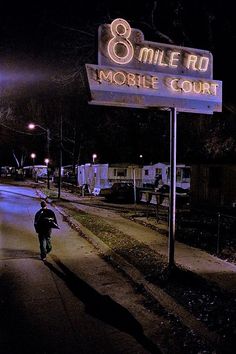 a man is walking down the street in front of a mobile court sign at night