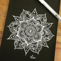 a pen is sitting on top of a black notebook with a white drawing of a flower