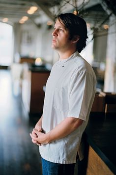 a man standing in front of a wooden counter with his hands folded up and looking off to the side