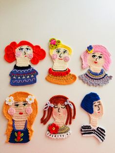 six crocheted dolls are arranged on a white surface, each with different faces