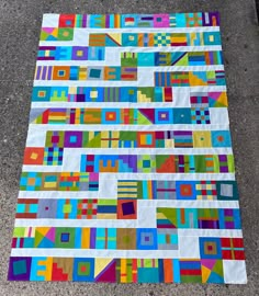 a multicolored quilt is laying on the ground with it's squares and rectangles