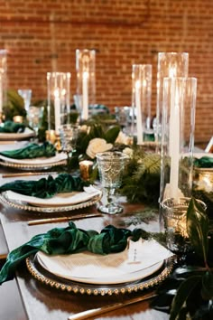 the table is set with candles, plates and greenery for an elegant dinner party