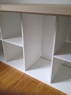 a white shelf with several open shelves on the top and bottom, sitting on a hard wood floor