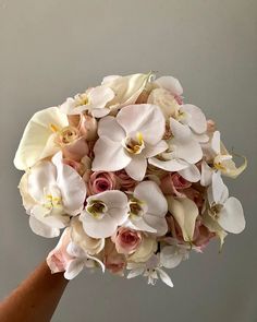 a person holding a bouquet of white and pink flowers in their left hand, against a gray background