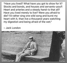 a man sitting on top of a wooden bench in front of a wall with words above it