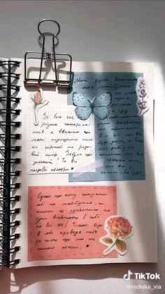 an open notebook with paper clips and butterflies on the pages, next to a pink flower