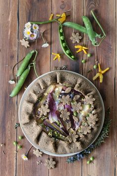 a bowl filled with food sitting on top of a wooden table next to flowers and pea pods