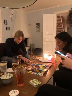 three people sitting around a table with drinks and magazines on it, looking at their cell phones