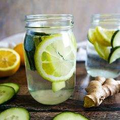 two mason jars filled with lemon, cucumber and lime slices on top of a wooden table