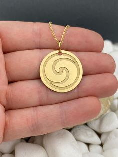 a hand holding a gold pendant with a spiral design on it's front and back