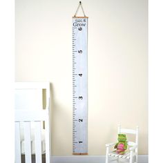 a wooden growth chart hanging on the wall next to a white rocking chair and baby's crib