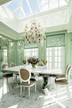 an elegant dining room with green walls and chandelier above the white table surrounded by beige upholstered chairs