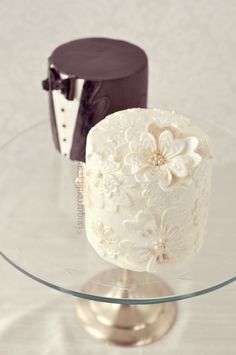 two wedding cakes sitting on top of a glass table next to each other, decorated with flowers and tuxedos