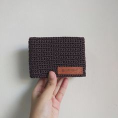 a hand is holding a crocheted wallet with a leather tag on it's side