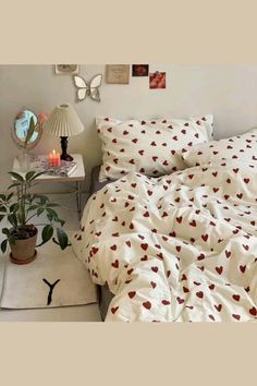 a bed with white sheets and red hearts on it, next to a small table with a potted plant