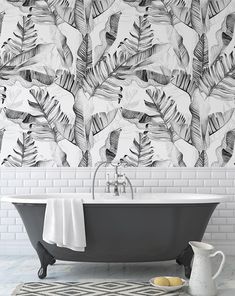 a bath tub sitting next to a white brick wall with black and white leaves on it