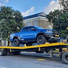 a blue truck is on the back of a flatbed trailer