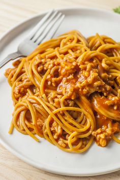 a white plate topped with spaghetti covered in sauce and meat next to a silver fork