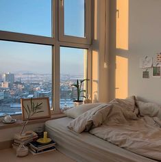 an unmade bed sitting in front of two large windows with city view behind it