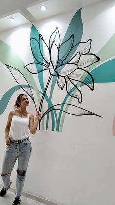 a woman standing in front of a flower painted on the wall