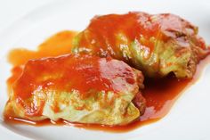 two stuffed cabbages covered in sauce on a white plate