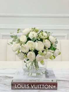 a bouquet of white roses in a glass vase on top of a stack of books