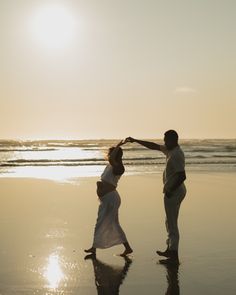 a man and woman dancing on the beach at sunset