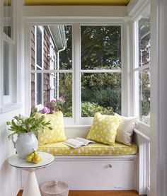 a white window seat sitting under a yellow painted skylight next to a table with flowers on it