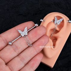 a person holding two piercings in their hand, one is shaped like a butterfly and the other has a chain attached to it