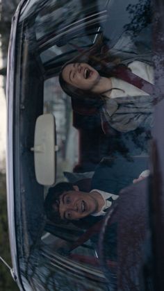 two people are looking out the window of a vehicle and smiling at something in the distance