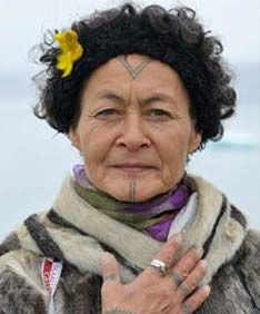 an older woman with tattoos on her face and neck standing in front of the ocean