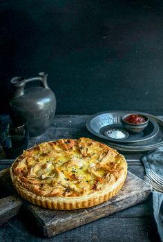 a quiche sitting on top of a wooden cutting board next to plates and silverware