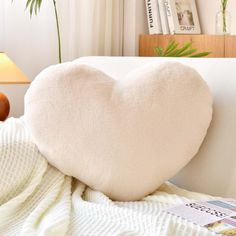 a white heart shaped pillow sitting on top of a bed next to a lamp and table