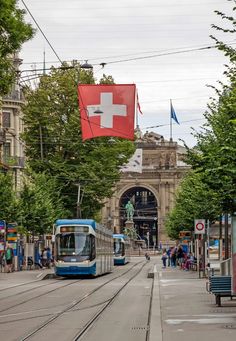 two trains on the tracks in front of a building with a swiss flag hanging from it's roof