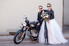 a man and woman standing next to a motorcycle with flowers on the bike's tail