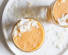 two glasses filled with orange smoothie on top of a white plate and garnished with coconut flakes