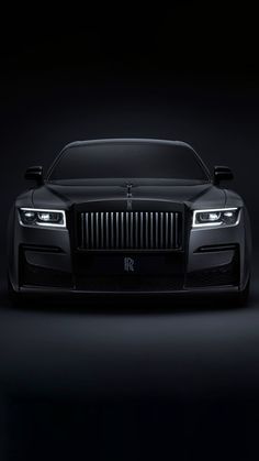 the front end of a black rolls royce on a dark background with light coming from behind