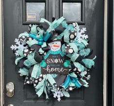 a wreath that says snow is home on the front door with a snowman and black polka dot bow