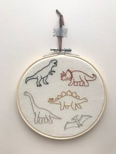 a white wall with some embroidery on it that has different types of dinosaurs in it