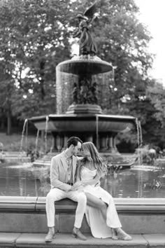 a man and woman sitting next to each other on a bench in front of a fountain