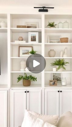 a living room with white bookcases and potted plants on the shelves in front of it