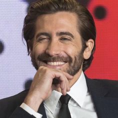 a man in a suit and tie smiles at the camera with his hand on his chin