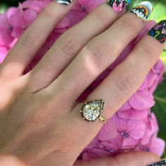 a woman's hand with colorful nail polish holding a ring on her finger and flowers in the background