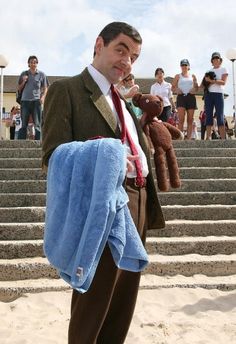 a man is standing on the beach with a teddy bear in his jacket and tie