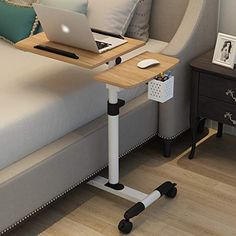 a laptop computer sitting on top of a wooden table next to a bed with white pillows