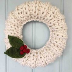 a knitted wreath hanging on the front door with two red flowers and green leaves